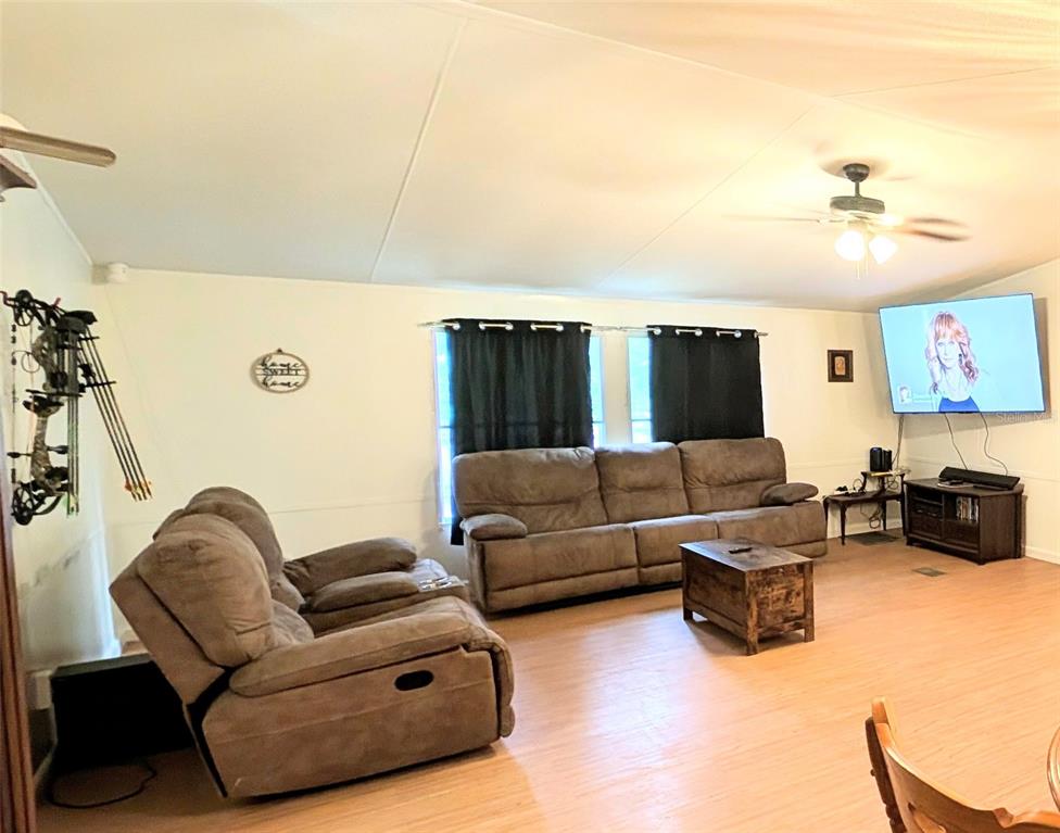 A living room features light wood-look flooring, a brown sofa, a recliner, and a television — 23880 NE 121ST LANE, FORT MC COY, FL