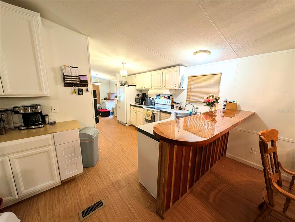 A kitchen with white cabinets, wood-look flooring, and a raised wooden breakfast bar — 23880 NE 121ST LANE, FORT MC COY, FL