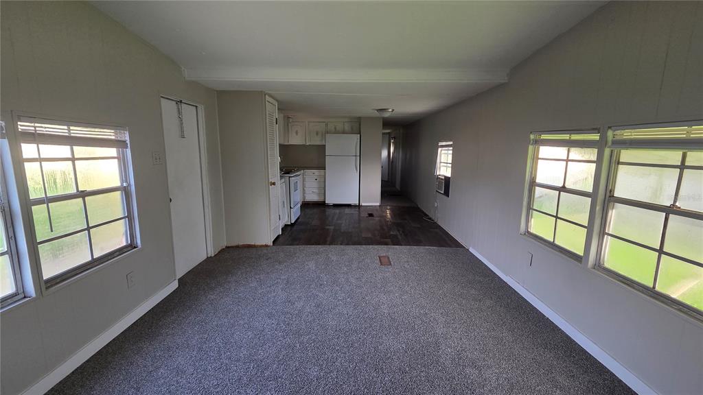 A living room with gray carpet leads to a kitchen featuring white appliances and dark flooring — 2735 W 10TH STREET UNIT 1, LAKELAND, FL