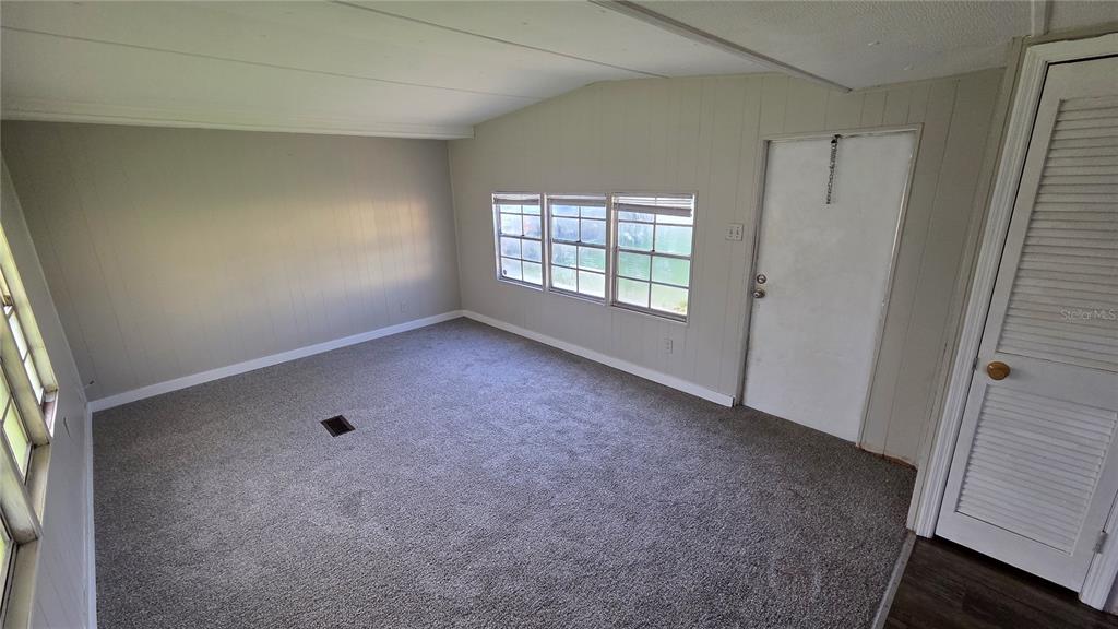 An empty room with gray carpet, paneled walls, three windows, and a white door — 2735 W 10TH STREET UNIT 1, LAKELAND, FL