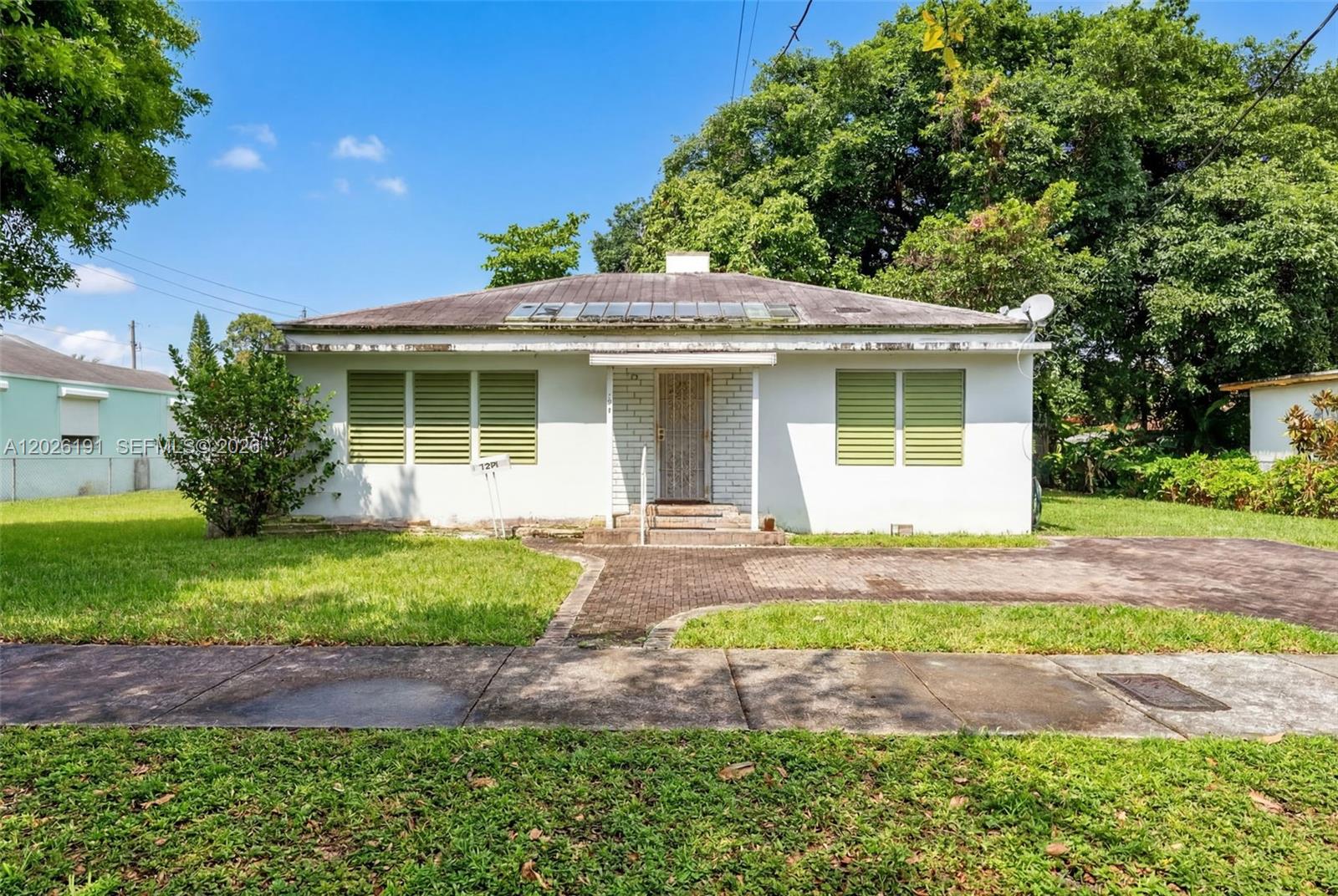 A single-story white house with a hip roof and green shutters sits on a lawn — 1279 NW 41st St, Miami FL 33142, MIAMI, FL