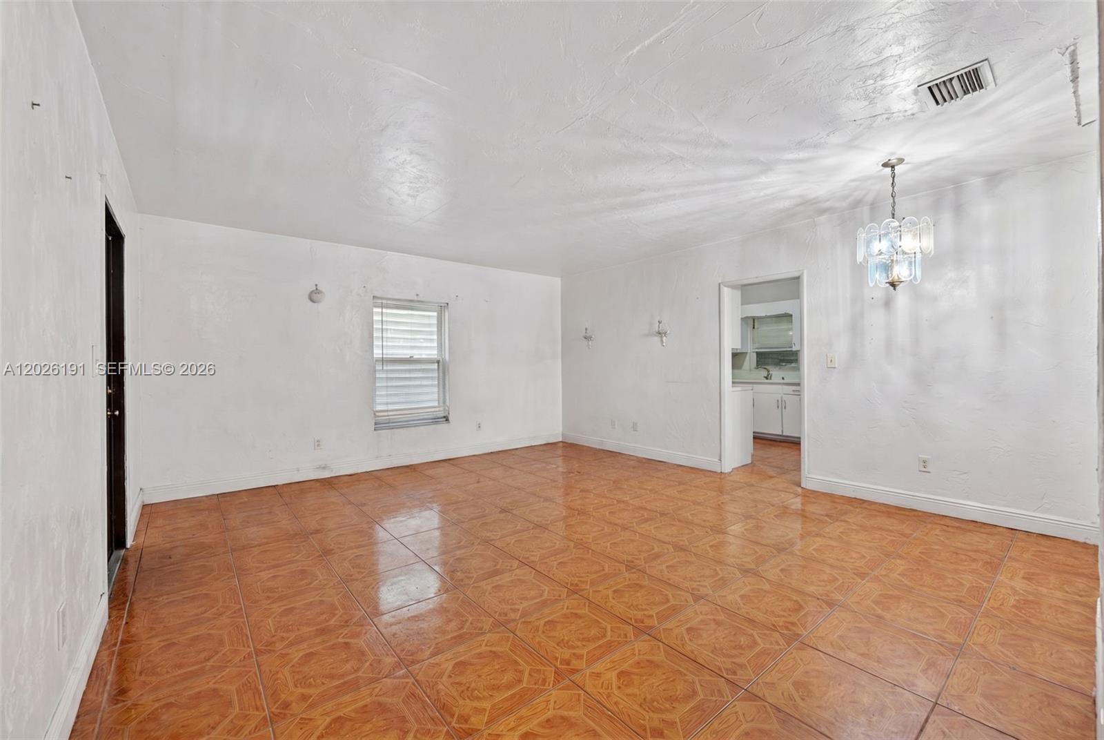 An empty room features white textured walls, orange patterned tile flooring, and a crystal chandelier — 1279 NW 41st St, Miami FL 33142, MIAMI, FL