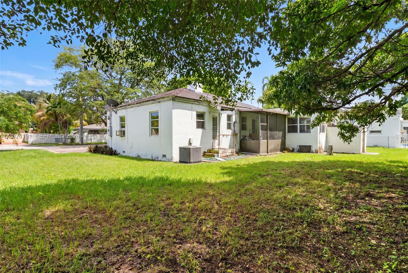 The rear exterior of a white, single-story house features a screened porch and grassy yard — 1279 NW 41st St, Miami FL 33142, MIAMI, FL