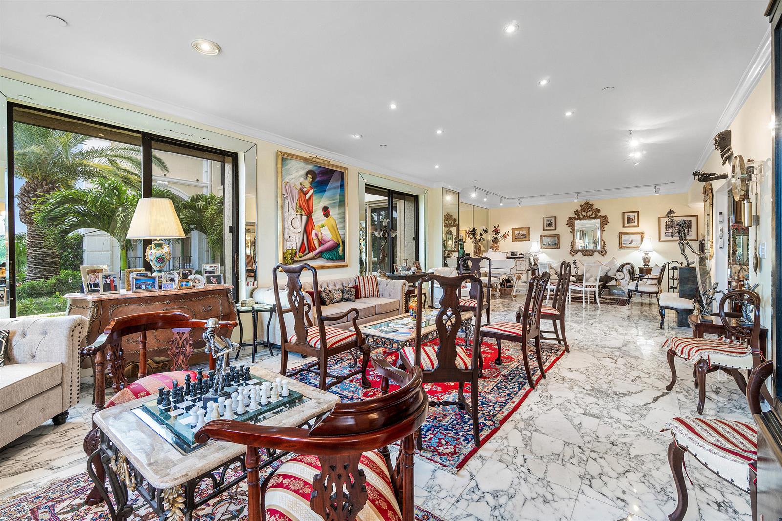 A spacious living room features marble floors, ornate wooden furniture, a chess set, and large windows — 150 Bradley Place # 101, Palm Beach FL 33480, PALM BEACH, FL
