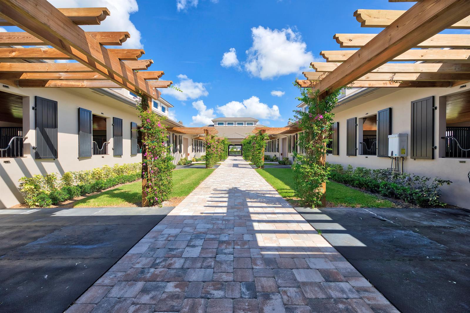 A stone walkway leads between two rows of horse stalls with wooden pergolas and landscaping — 5219 130th Avenue S, Wellington FL 33449, WELLINGTON, FL