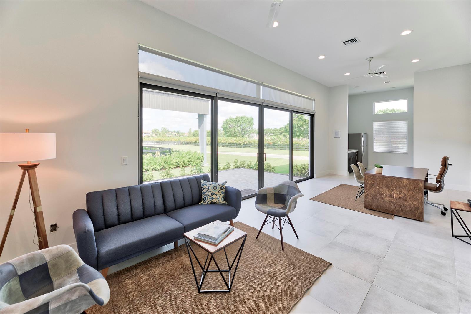 A modern living and office space features a blue sofa, desk, and large sliding glass doors — 5219 130th Avenue S, Wellington FL 33449, WELLINGTON, FL