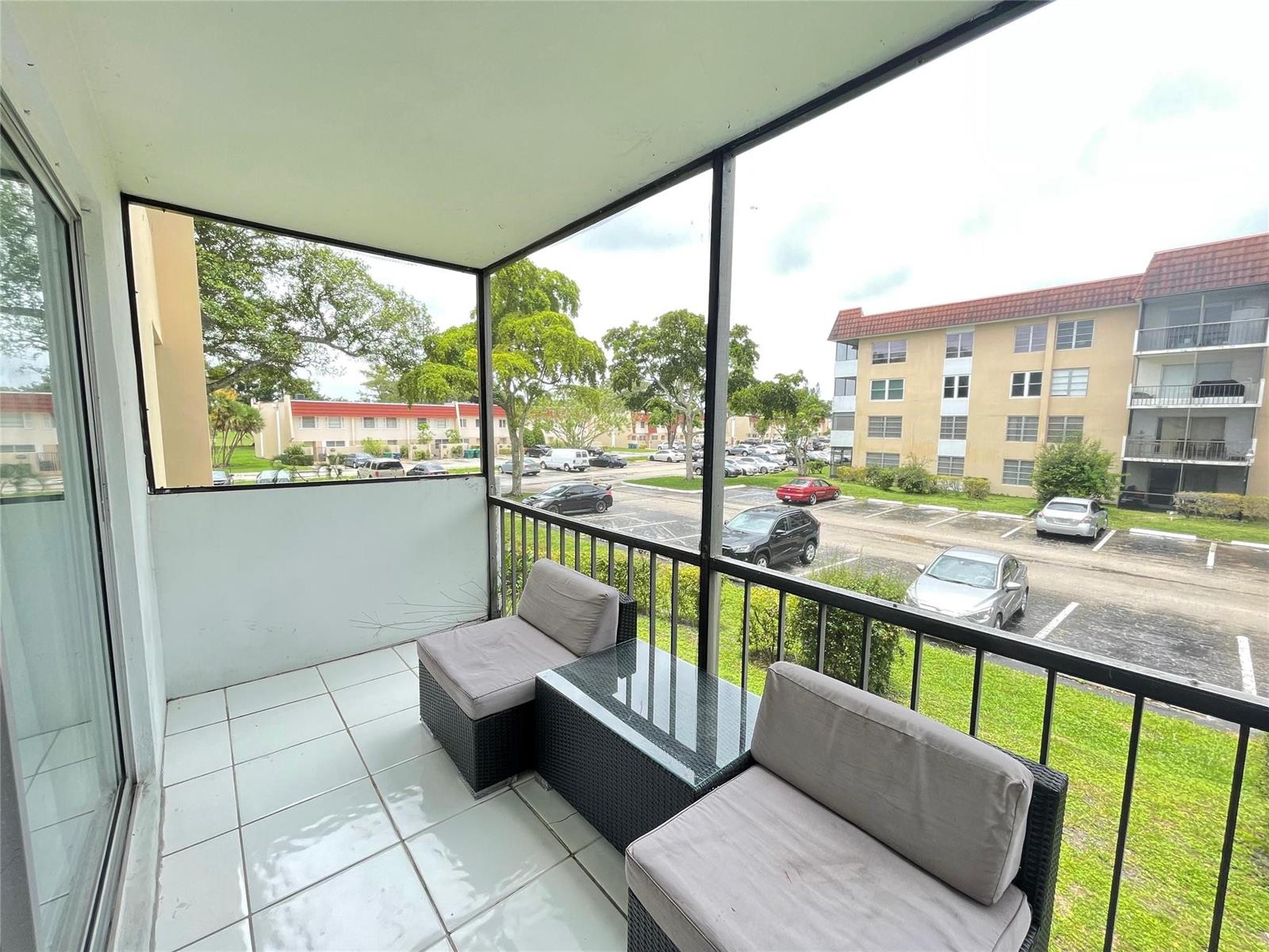 A tiled balcony features two wicker chairs with cushions and a view of a parking lot — 4156 Inverrary Drive # 204, Lauderhill FL 33319, LAUDERHILL, FL