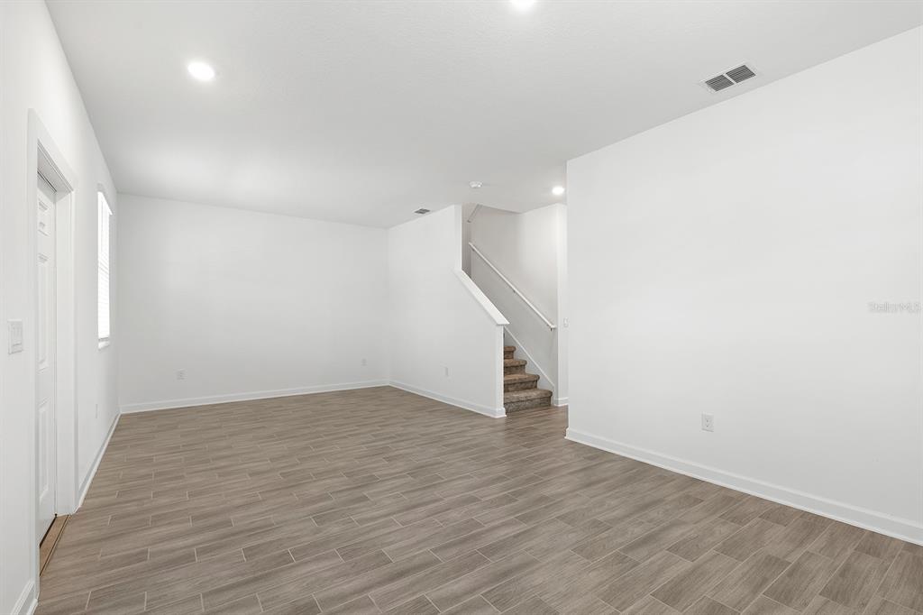 An empty room with white walls, light wood-look tile flooring, and a carpeted staircase — 3039 ELLA WAY, ST CLOUD, FL