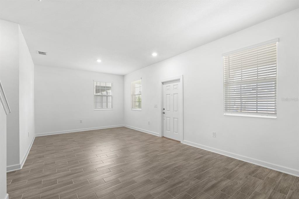 An empty room with white walls, wood-look tile flooring, and several windows with blinds — 3039 ELLA WAY, ST CLOUD, FL