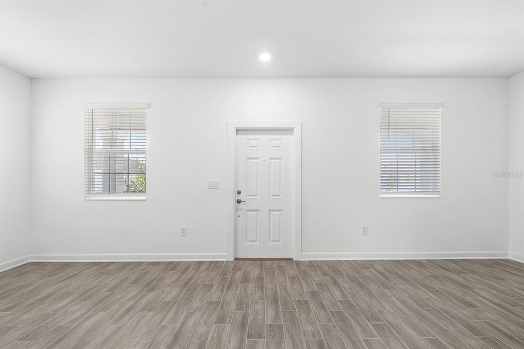 A bright room with white walls, wood-look tile flooring, two windows, and a central door — 3039 ELLA WAY, ST CLOUD, FL