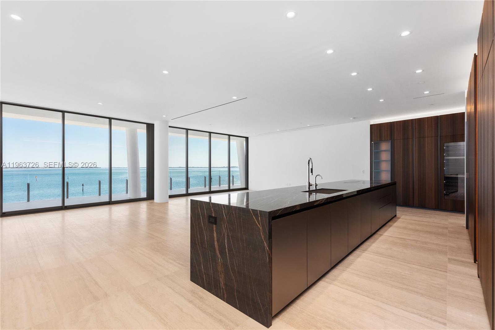 A modern kitchen features a dark marble island and wood cabinetry overlooking the ocean — 5 Grove Isle Dr # M303, Miami FL 33133, MIAMI, FL
