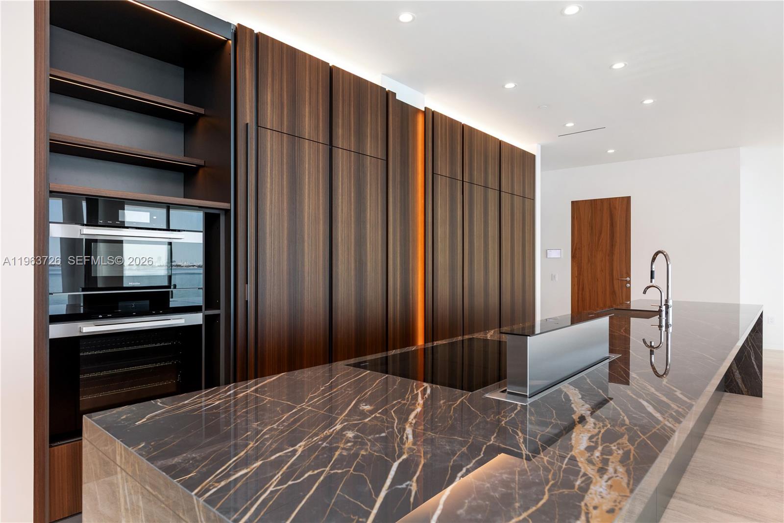 A modern kitchen features dark wood cabinetry, a marble island with a downdraft vent, and appliances — 5 Grove Isle Dr # M303, Miami FL 33133, MIAMI, FL