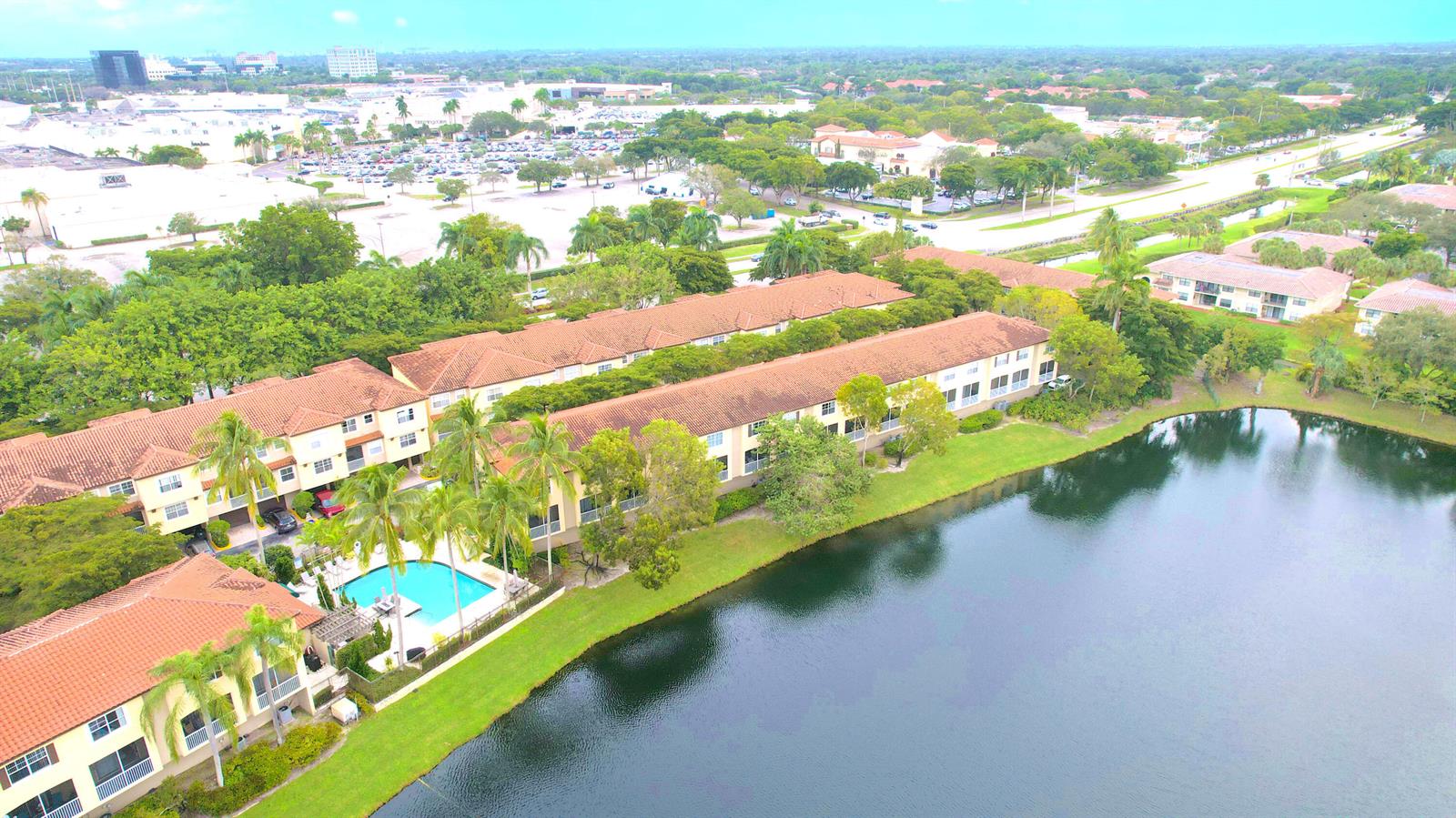 An aerial view shows multi-story apartment buildings with tile roofs situated beside a large lake — 20889 Saint Andrews Boulevard, Boca Raton FL 33433, BOCA RATON, FL