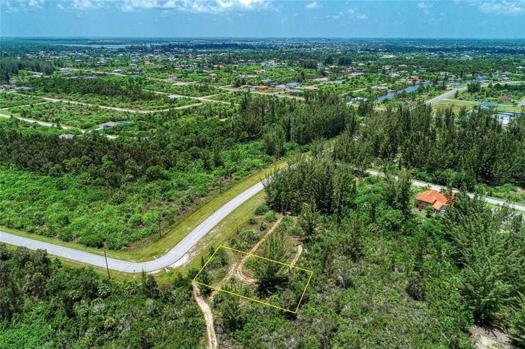An aerial view shows a vacant, rectangular lot outlined in yellow amidst dense green vegetation — 15286 INGRAHAM BOULEVARD, PORT CHARLOTTE, FL