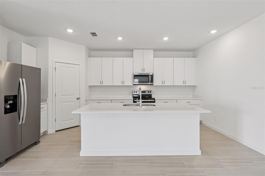 A modern kitchen features white cabinets, stainless steel appliances, and a central island with quartz — 14 DILLY COURT, PALM COAST, FL