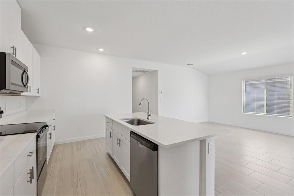 A modern kitchen features white cabinets, a central island with a sink, and light flooring — 14 DILLY COURT, PALM COAST, FL