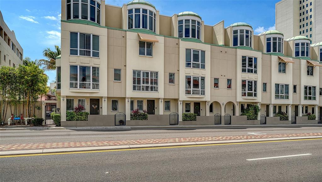 A row of multi-story townhomes with arched windows and tan facades sits along a street — 235 COCOANUT AVENUE UNIT 106-B, SARASOTA, FL