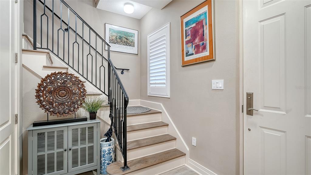 An entryway features a staircase with a black metal railing, a gray cabinet, and artwork — 235 COCOANUT AVENUE UNIT 106-B, SARASOTA, FL