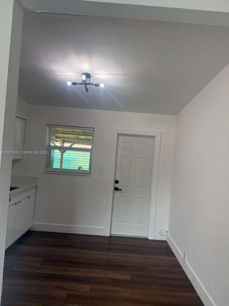 A kitchen features white cabinets, dark wood-look flooring, a window, and a white door — 2029 Washington Ave # 2, Opa-Locka FL 33054, OPA-LOCKA, FL