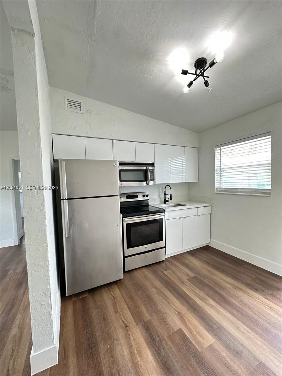 A kitchen features white flat-panel cabinets, stainless steel appliances, and wood-look flooring — 2029 Washington Ave # 2, Opa-Locka FL 33054, OPA-LOCKA, FL