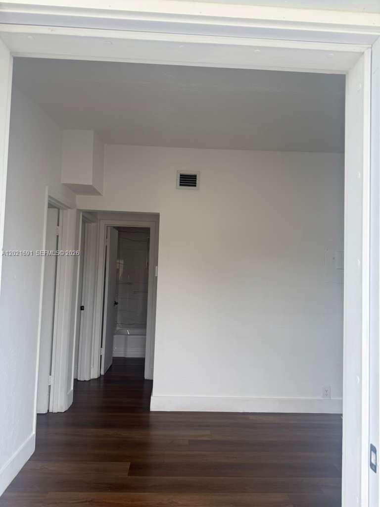 An interior view shows a room with dark wood flooring leading to a hallway and bathroom — 2029 Washington Ave # 2, Opa-Locka FL 33054, OPA-LOCKA, FL