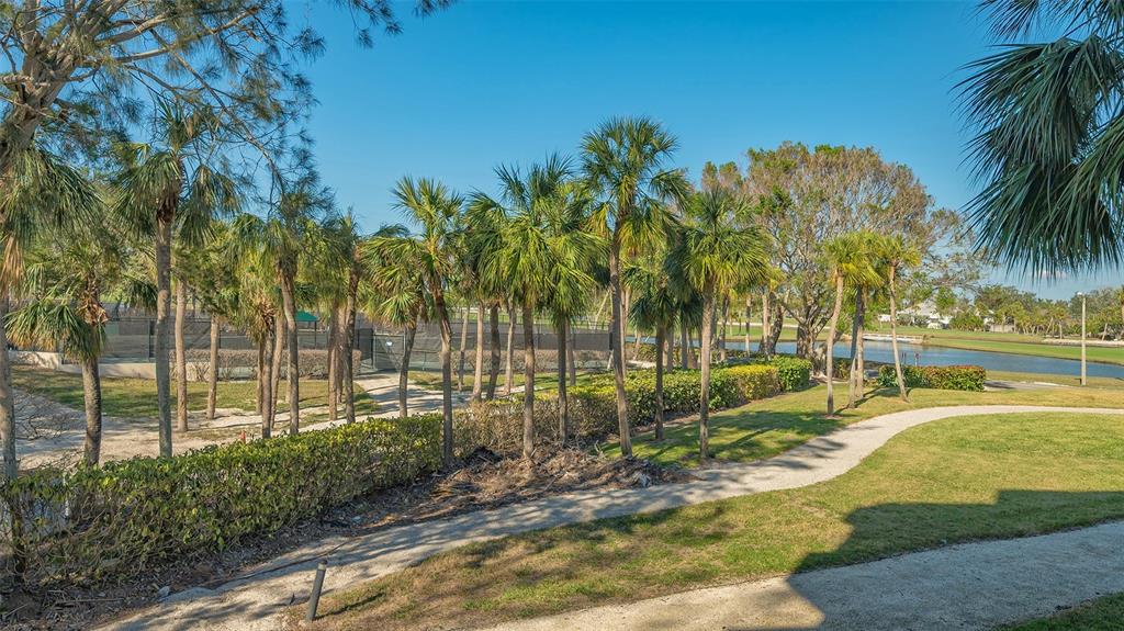 A paved path winds through a grassy area with palm trees and a tennis court — 250 SANDS POINT ROAD UNIT 5101, LONGBOAT KEY, FL