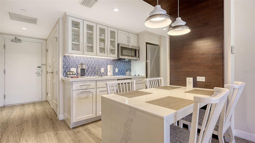 A kitchen with white cabinets, a blue patterned backsplash, and a dining table with chairs — 250 SANDS POINT ROAD UNIT 5101, LONGBOAT KEY, FL