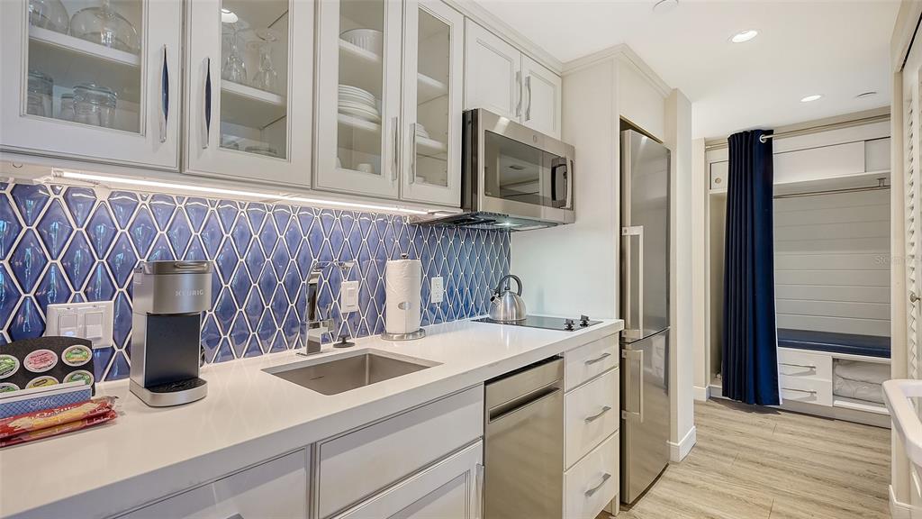 A kitchen features white cabinets, a blue diamond-patterned backsplash, stainless steel appliances, and wood flooring — 250 SANDS POINT ROAD UNIT 5101, LONGBOAT KEY, FL