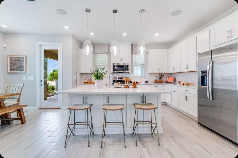 A bright kitchen features white cabinetry, a central island with bar stools, and stainless appliances — 5162 DOMINION ALLEY, ST CLOUD, FL