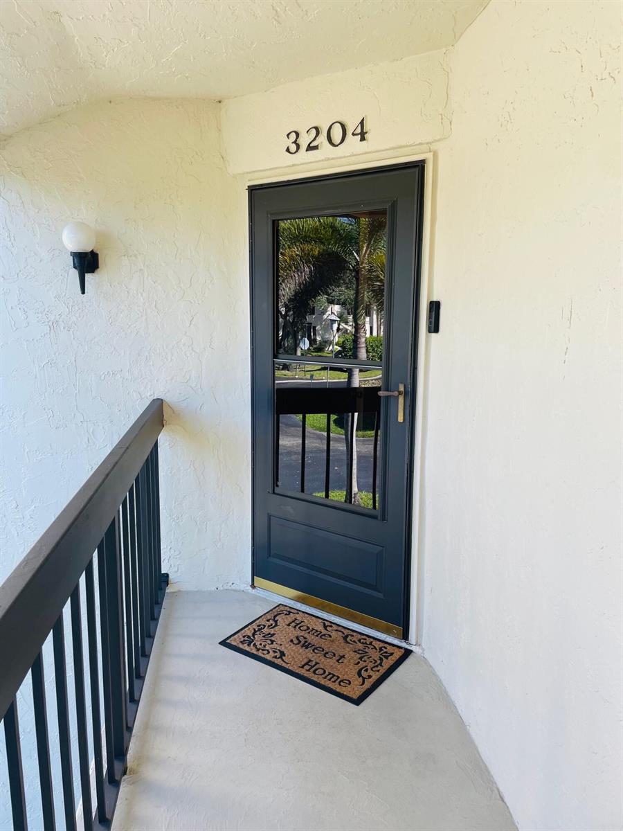 A dark-colored storm door with a glass panel is set in a white stucco wall — 3204 Perimeter Drive # 3204, FL 33467, FL