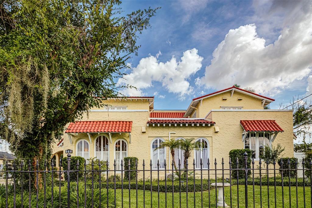 A yellow stucco house with a red tile roof stands behind a black metal fence — 845 E EDGEWOOD DRIVE, LAKELAND, FL