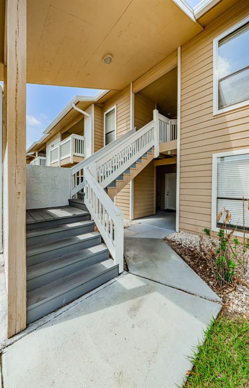 An exterior view of an apartment building featuring a wooden staircase leading to an upper balcony — 455 ALT 19 S UNIT 214, PALM HARBOR, FL