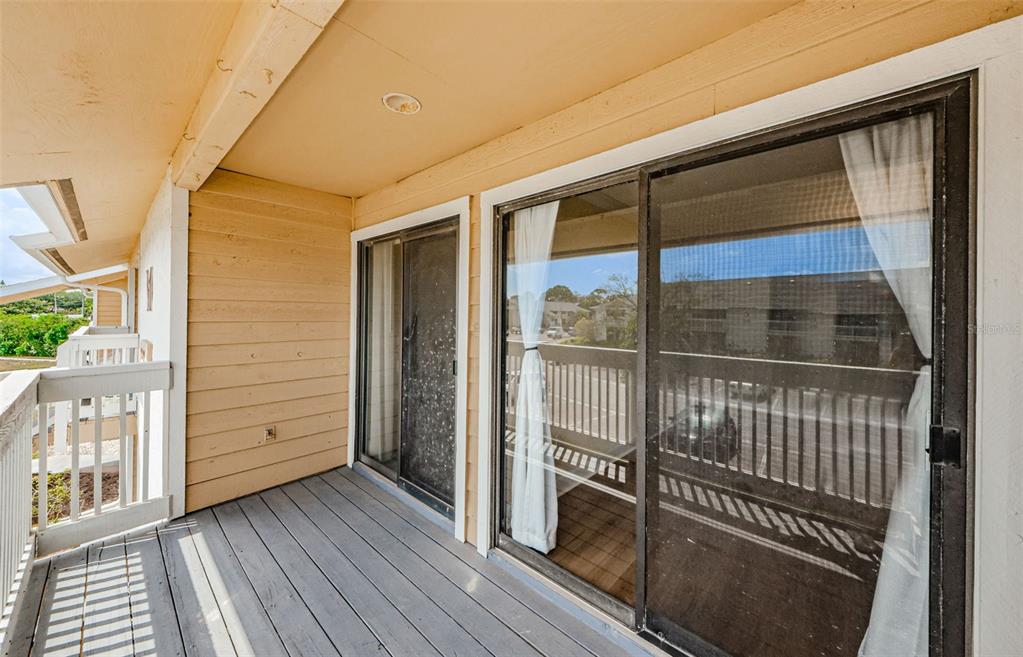 A balcony with gray wooden decking, light-colored siding, and sliding glass doors — 455 ALT 19 S UNIT 214, PALM HARBOR, FL