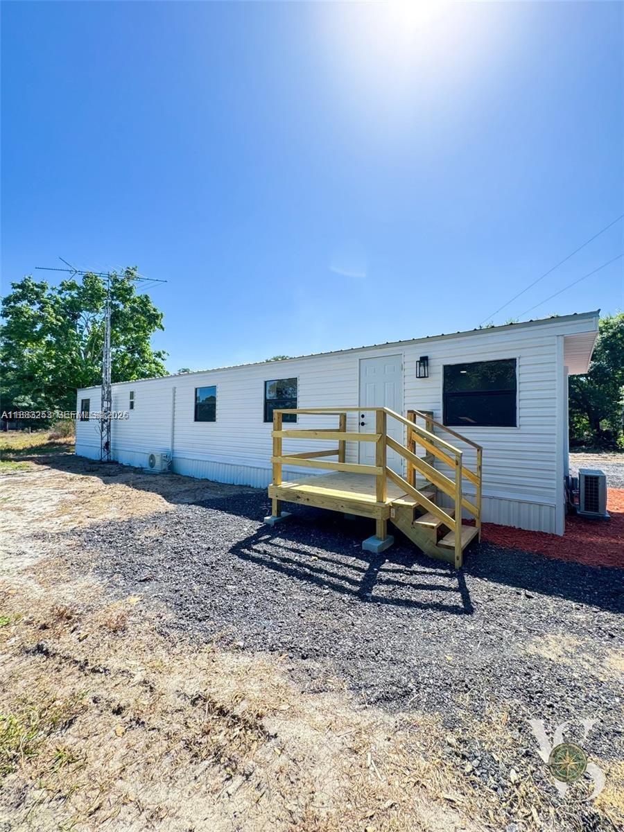 A white mobile home features a wooden deck with stairs and a metal antenna — 5121 PIONEER 18TH ST, Clewiston FL 33440, CLEWISTON, FL