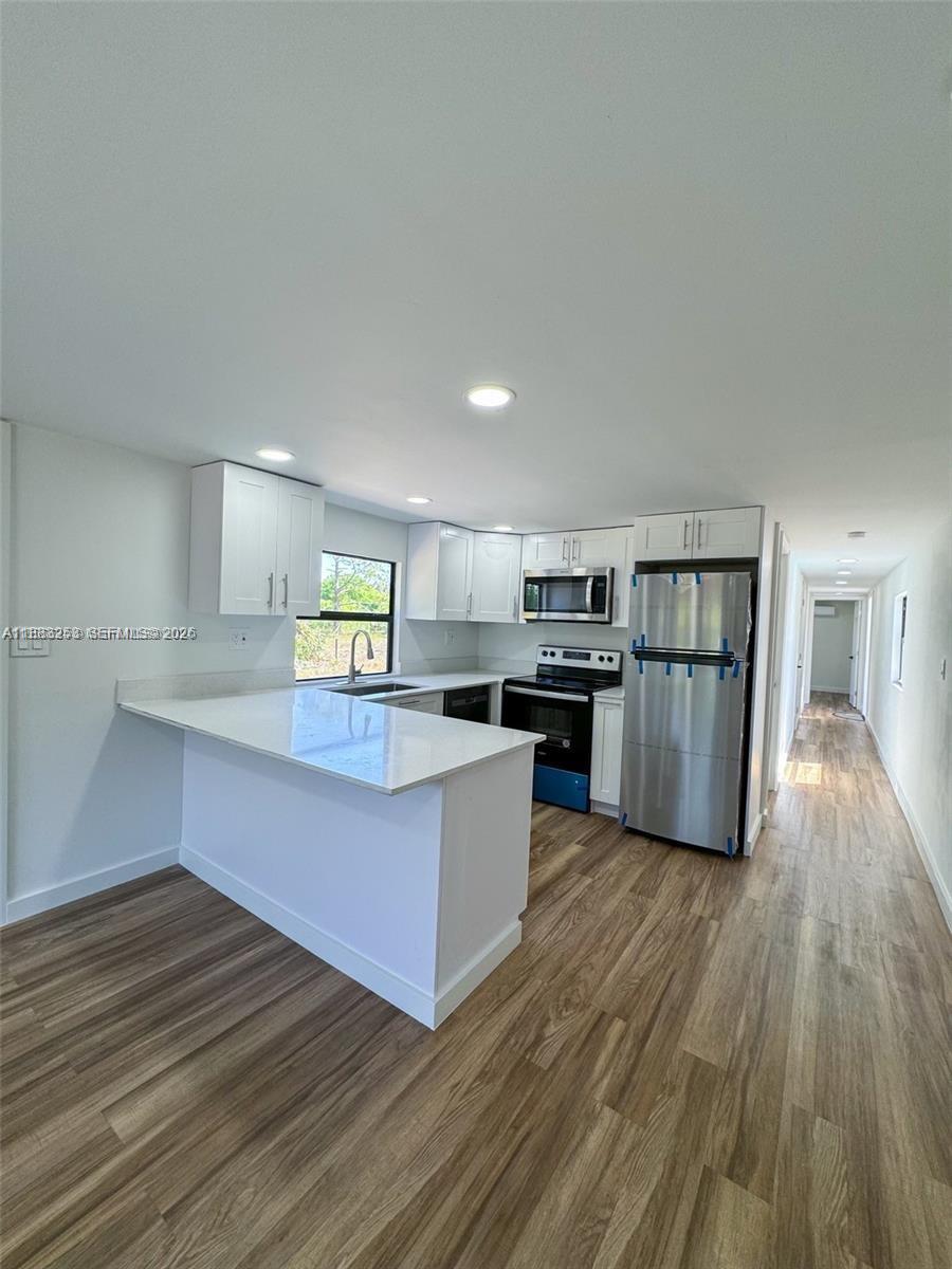A modern kitchen features white cabinets, stainless steel appliances, and a white quartz peninsula — 5121 PIONEER 18TH ST, Clewiston FL 33440, CLEWISTON, FL