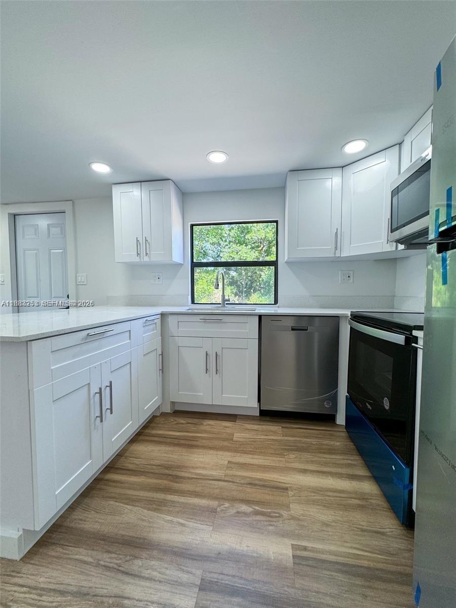 A renovated kitchen features white shaker cabinets, stainless steel appliances, and light wood-look flooring — 5121 PIONEER 18TH ST, Clewiston FL 33440, CLEWISTON, FL
