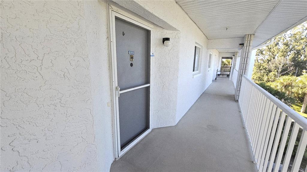 An exterior walkway leads to a gray door with a screen door in a building — 1401 S MCCALL ROAD UNIT 301A, ENGLEWOOD, FL