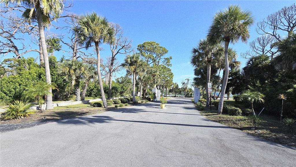 A paved driveway lined with palm trees leads toward a gated entrance near the water — 1401 S MCCALL ROAD UNIT 301A, ENGLEWOOD, FL