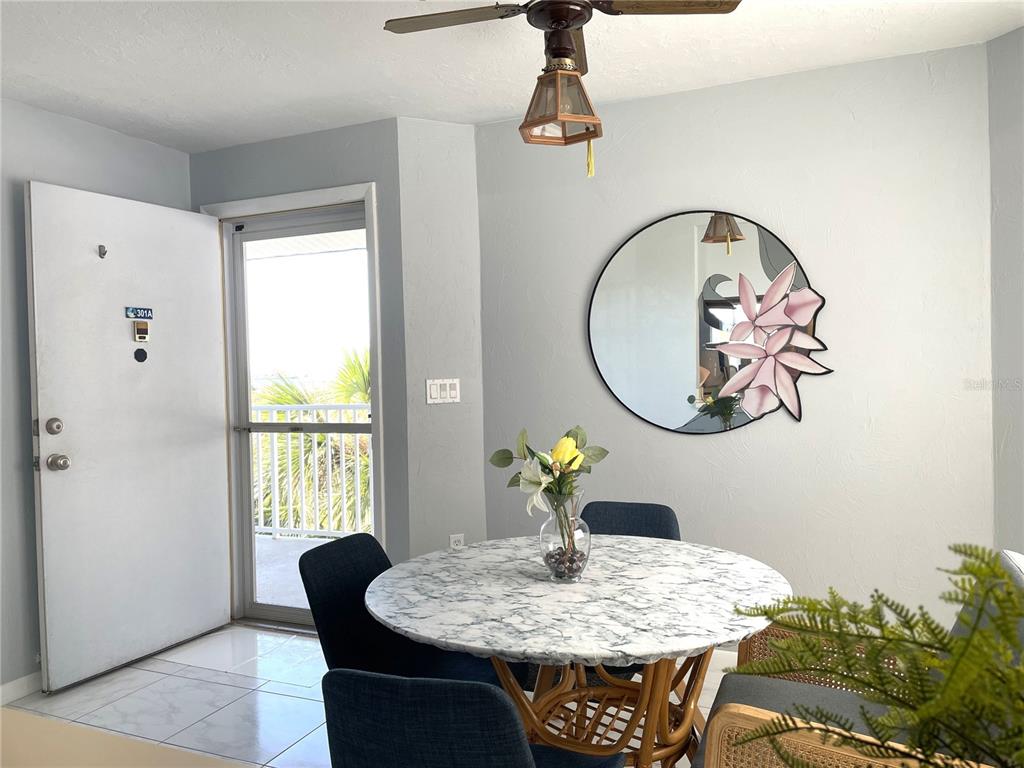 A dining area features a marble-topped table, blue chairs, a round mirror, and a door — 1401 S MCCALL ROAD UNIT 301A, ENGLEWOOD, FL