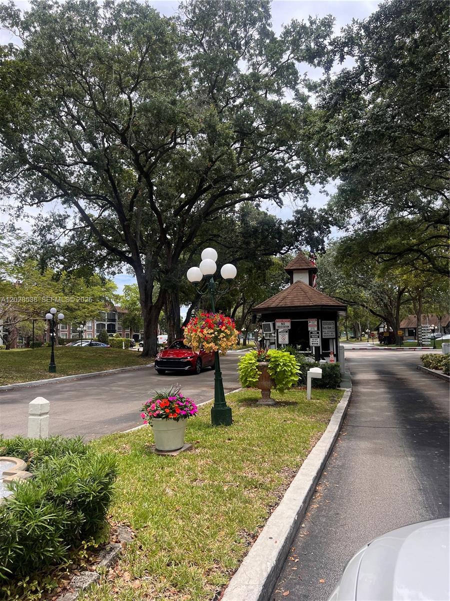 A gated community entrance features a guardhouse, mature trees, and a decorative lamp post — 3760 Inverrary Dr # 2A, Lauderhill FL 33319, LAUDERHILL, FL