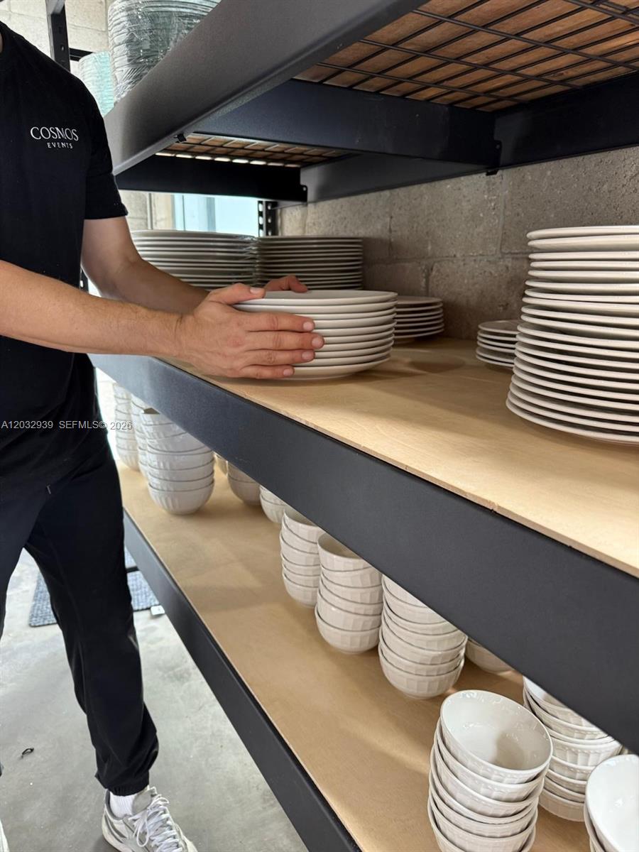 A person organizes stacks of white plates and bowls on metal shelving units — MEDLEY, FL