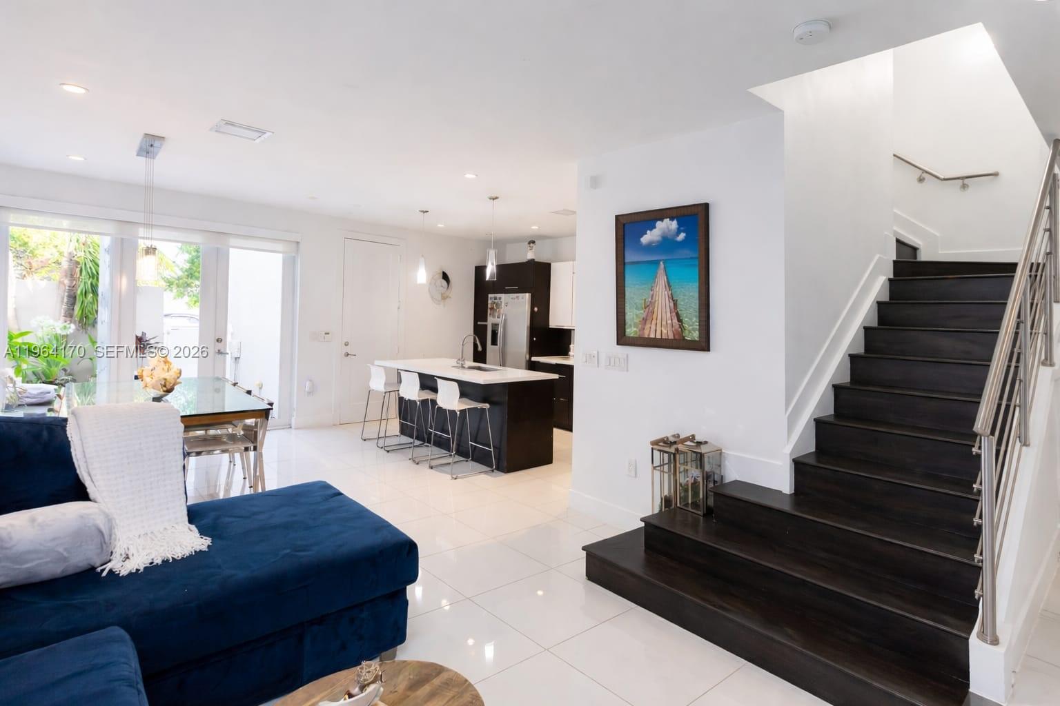 A modern open-concept living area features a kitchen with an island, dining space, and stairs — 10464 NW 66th St, Doral FL 33178, DORAL, FL