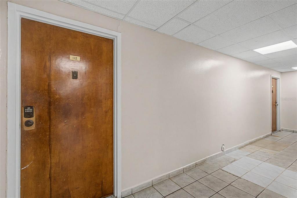 A hallway features a wooden door labeled 112, light-colored walls, and tiled flooring — 5055 NW 7TH STREET UNIT 112, MIAMI, FL