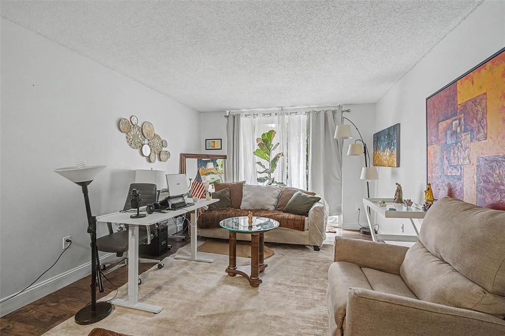 A living room features a desk, a sofa, an armchair, and a large abstract painting — 5055 NW 7TH STREET UNIT 112, MIAMI, FL