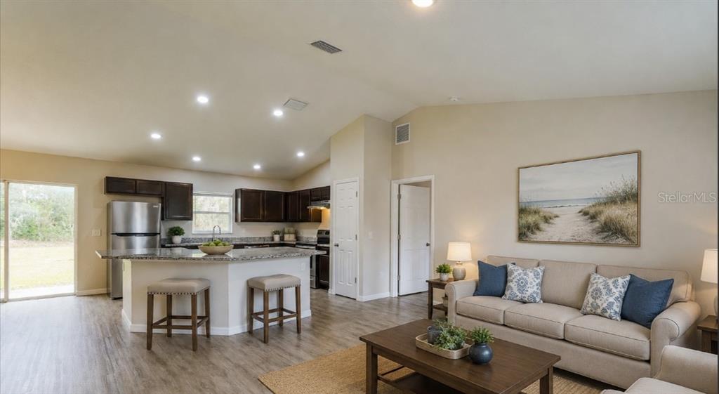 An open-concept kitchen and living area featuring dark wood cabinets, stainless appliances, and neutral furniture — 10 JUNIPER TRAIL, OCALA, FL