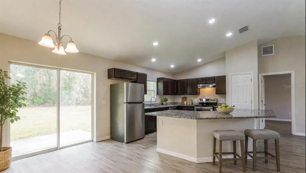 A kitchen with dark cabinets, granite countertops, stainless steel appliances, and a breakfast bar — 10 JUNIPER TRAIL, OCALA, FL