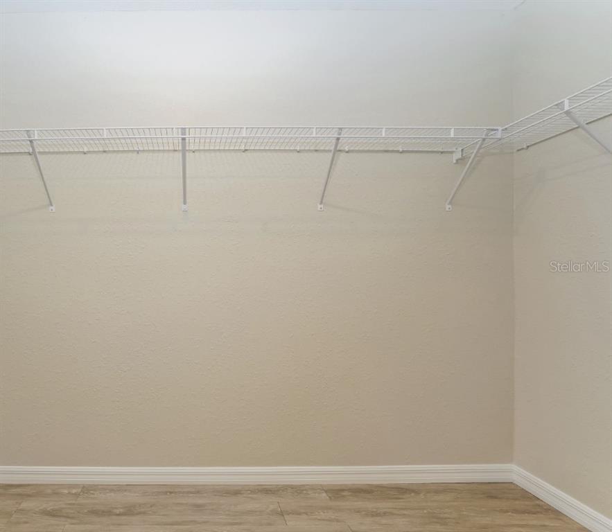 A walk-in closet features white wire shelving mounted on beige walls above wood-look flooring — 10 JUNIPER TRAIL, OCALA, FL