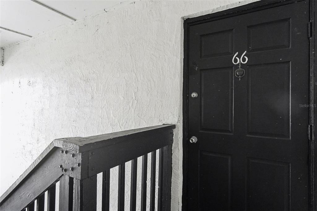 A black door labeled 66 is situated next to a wooden staircase railing — 2535 N ALAFAYA TRAIL UNIT 66, ORLANDO, FL