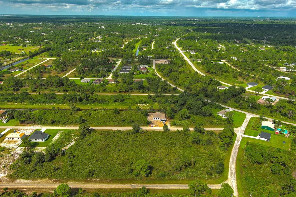 An aerial view shows a vacant lot surrounded by trees and scattered residential houses — 642 VASSER AVENUE S, LEHIGH ACRES, FL