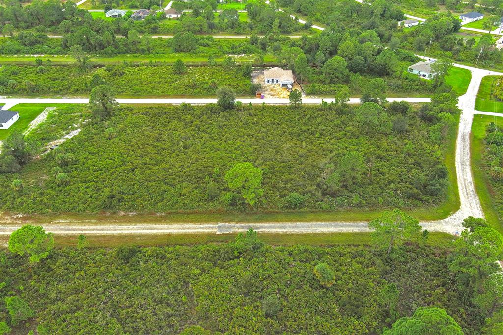 An aerial view shows a large, undeveloped wooded lot bordered by dirt roads and houses — 642 VASSER AVENUE S, LEHIGH ACRES, FL